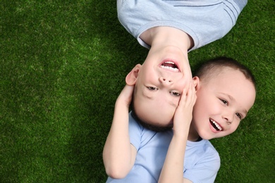 Photo of Portrait of cute twin brothers on green grass, top view. Space for text
