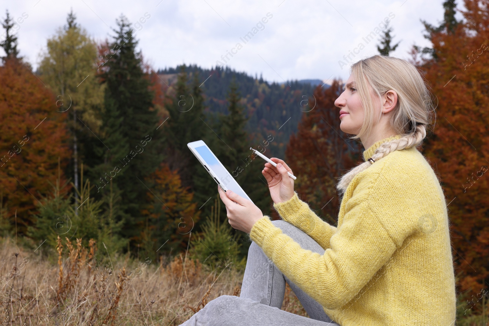 Photo of Young woman drawing with graphic tablet in mountains on autumn day