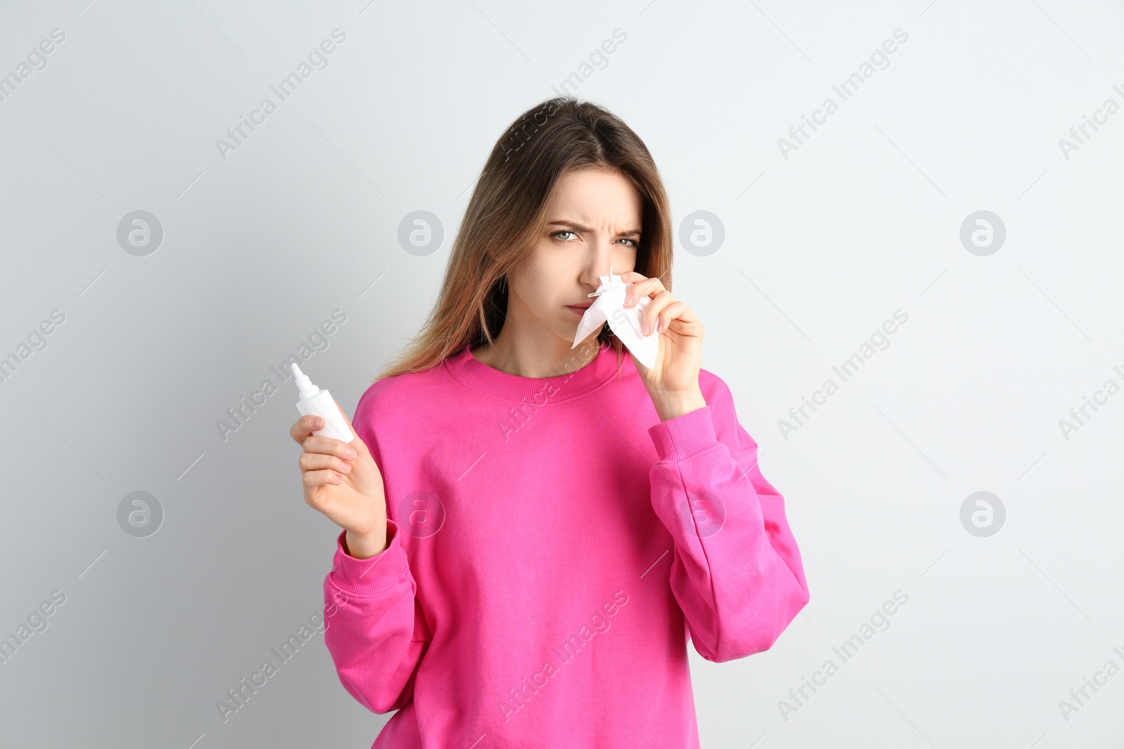 Photo of Sick young woman with nasal spray and tissue on white background