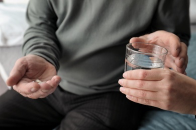Young woman giving water to senior man with pills, closeup