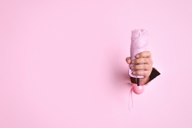 Woman holding bright foldable umbrella through hole in pink paper, closeup. Space for text