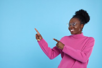 Photo of Beautiful young woman in eyeglasses pointing at something on light blue background. Space for text