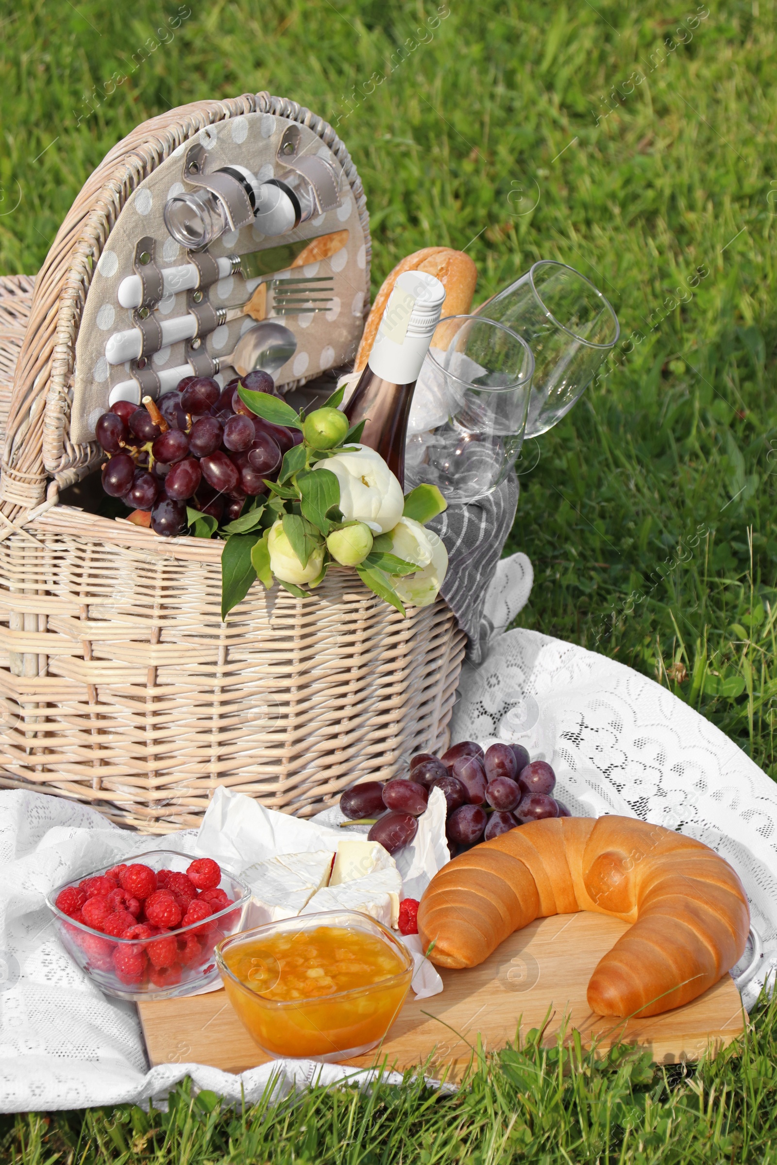 Photo of Picnic blanket with tasty food, flowers, basket and cider on green grass outdoors