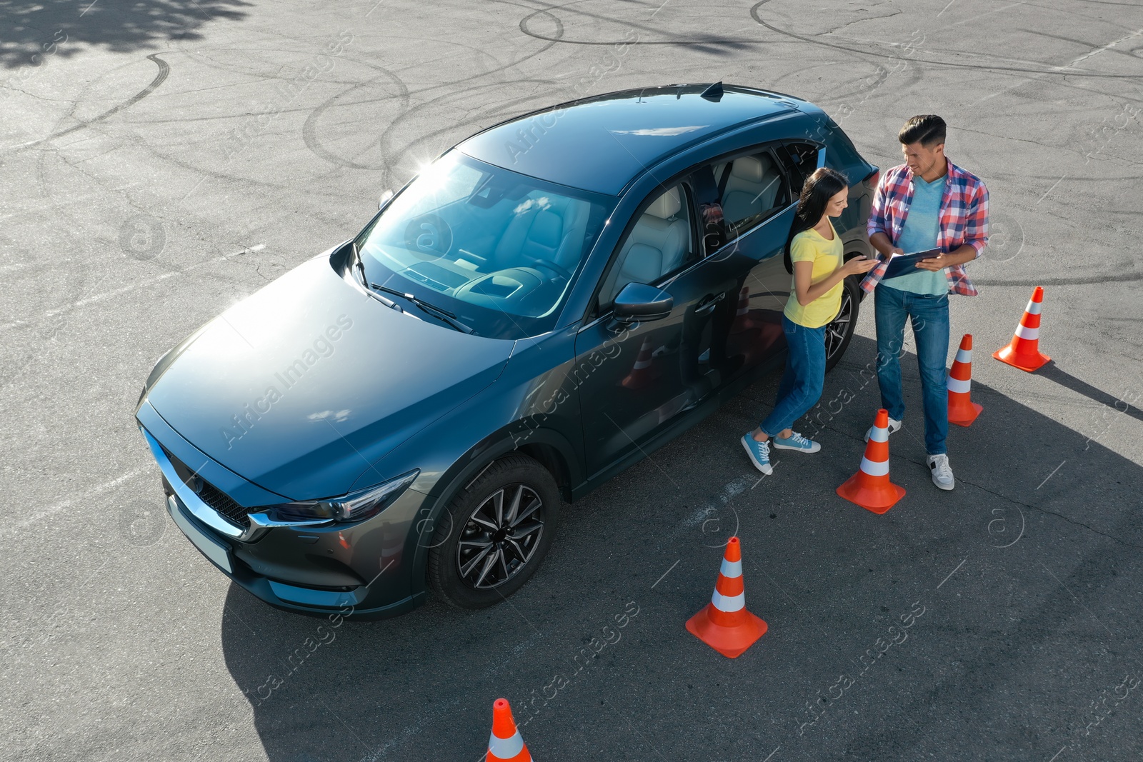 Photo of Instructor with clipboard near car and his student outdoors, above view. Driving school exam