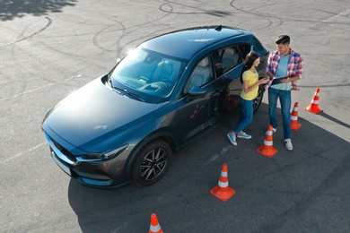 Instructor with clipboard near car and his student outdoors, above view. Driving school exam