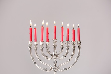 Silver menorah with burning candles against light grey background. Hanukkah celebration