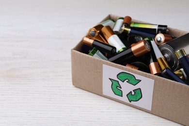 Used batteries in cardboard box with recycling symbol on white table, closeup. Space for text