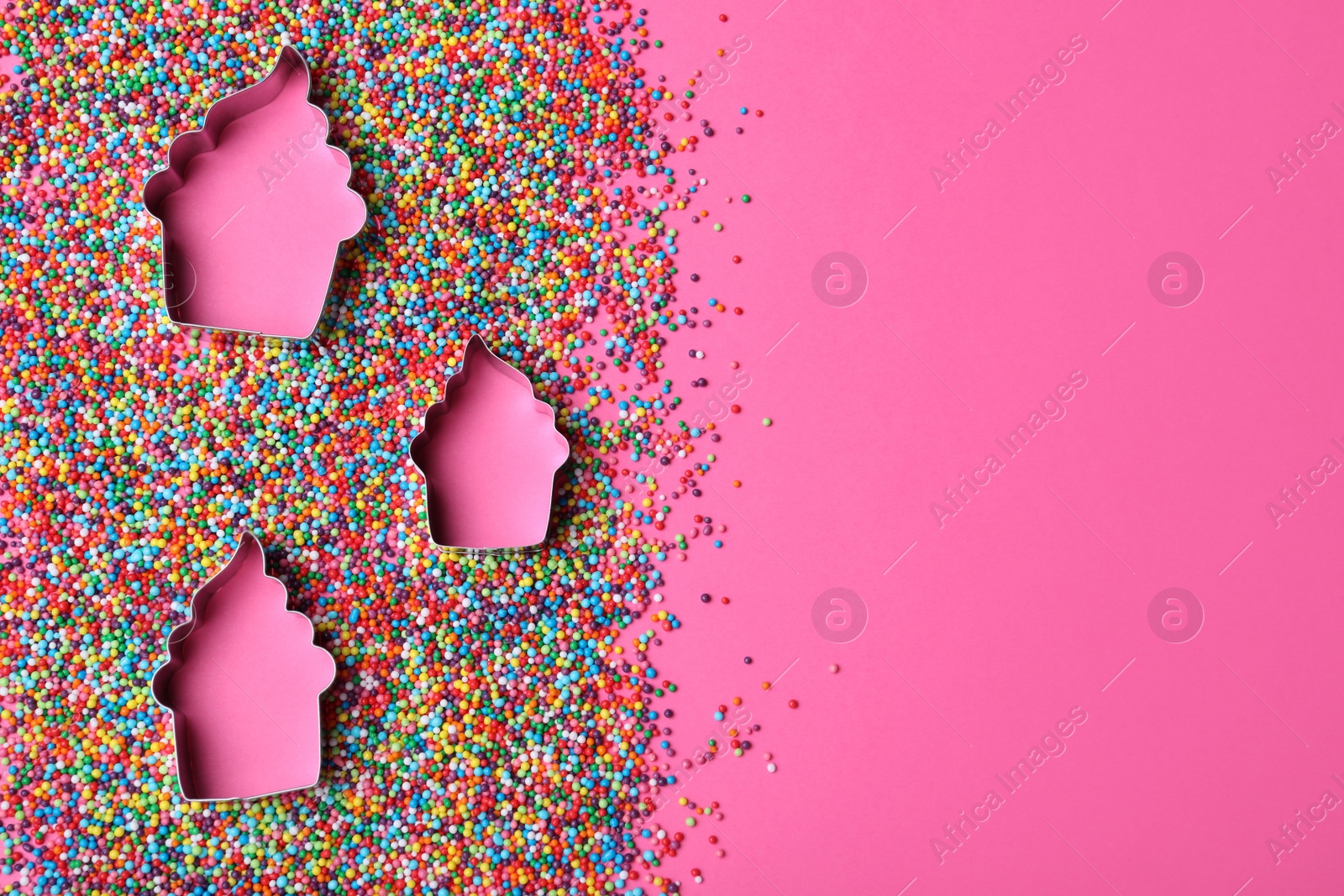 Photo of Cupcake shaped cookie cutters and sprinkles on pink background, flat lay with space for text. Confectionery decor