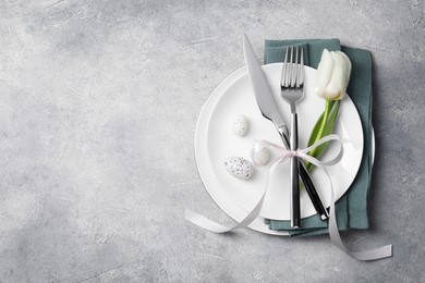 Festive table setting with painted eggs and white tulip on light grey background, top view with space for text. Easter celebration