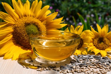 Photo of Sunflower oil in glass bowl and seeds on wooden table outdoors