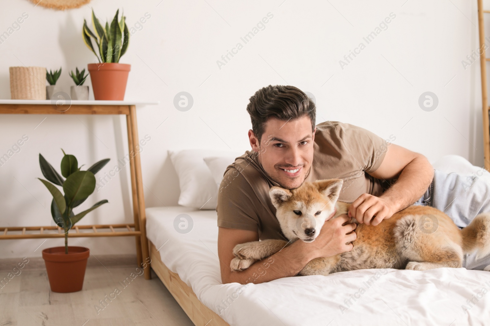 Photo of Man and Akita Inu dog in bedroom decorated with houseplants