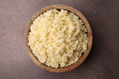 Photo of Tasty couscous in bowl on brown table, top view