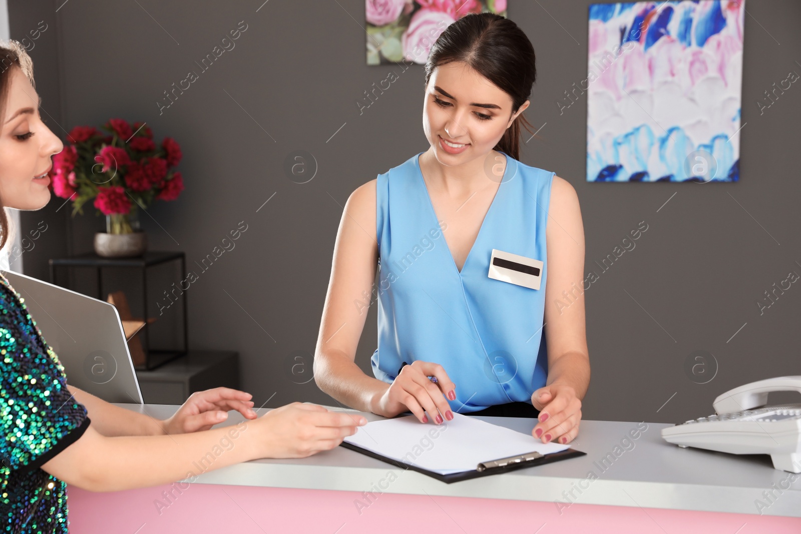 Photo of Young receptionist working with client at desk in beauty salon