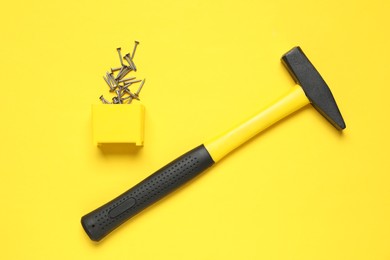 Photo of Hammer and metal nails on yellow background, top view