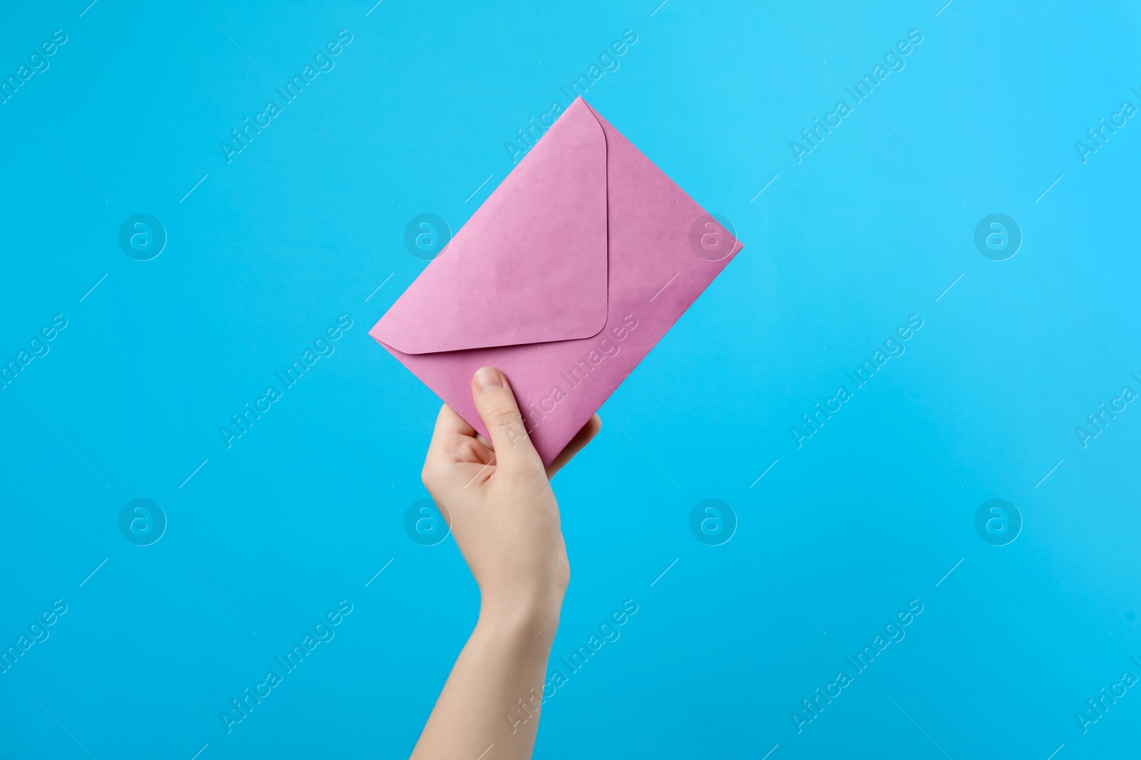 Photo of Woman holding pink paper envelope on light blue background, closeup