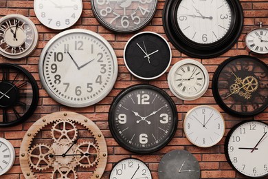 Photo of Collection of clocks hanging on red brick wall