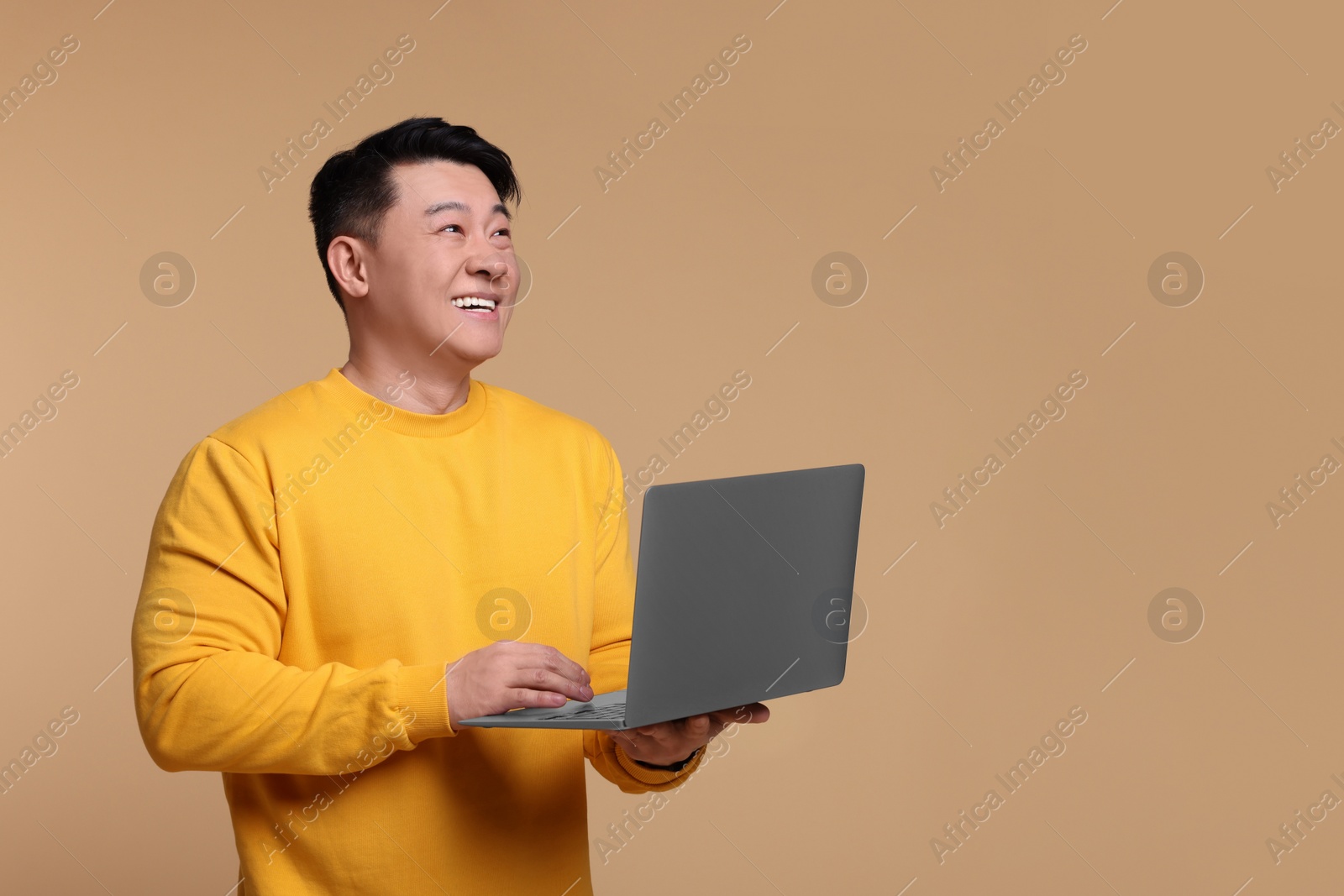 Photo of Happy man with laptop on beige background, space for text