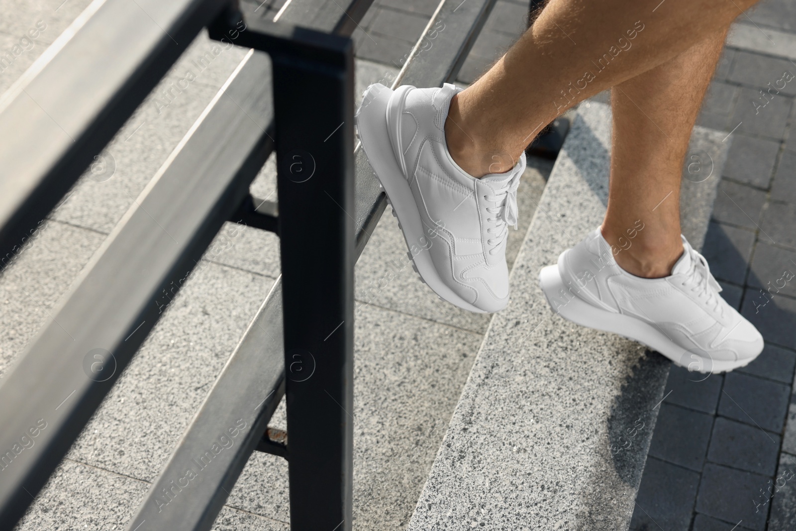 Photo of Man in stylish sneakers sitting on railing outdoors, closeup