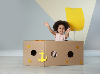 Cute African American child playing with cardboard ship near color wall