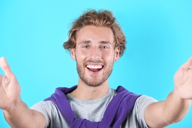 Photo of Handsome young man laughing and taking selfie on color background