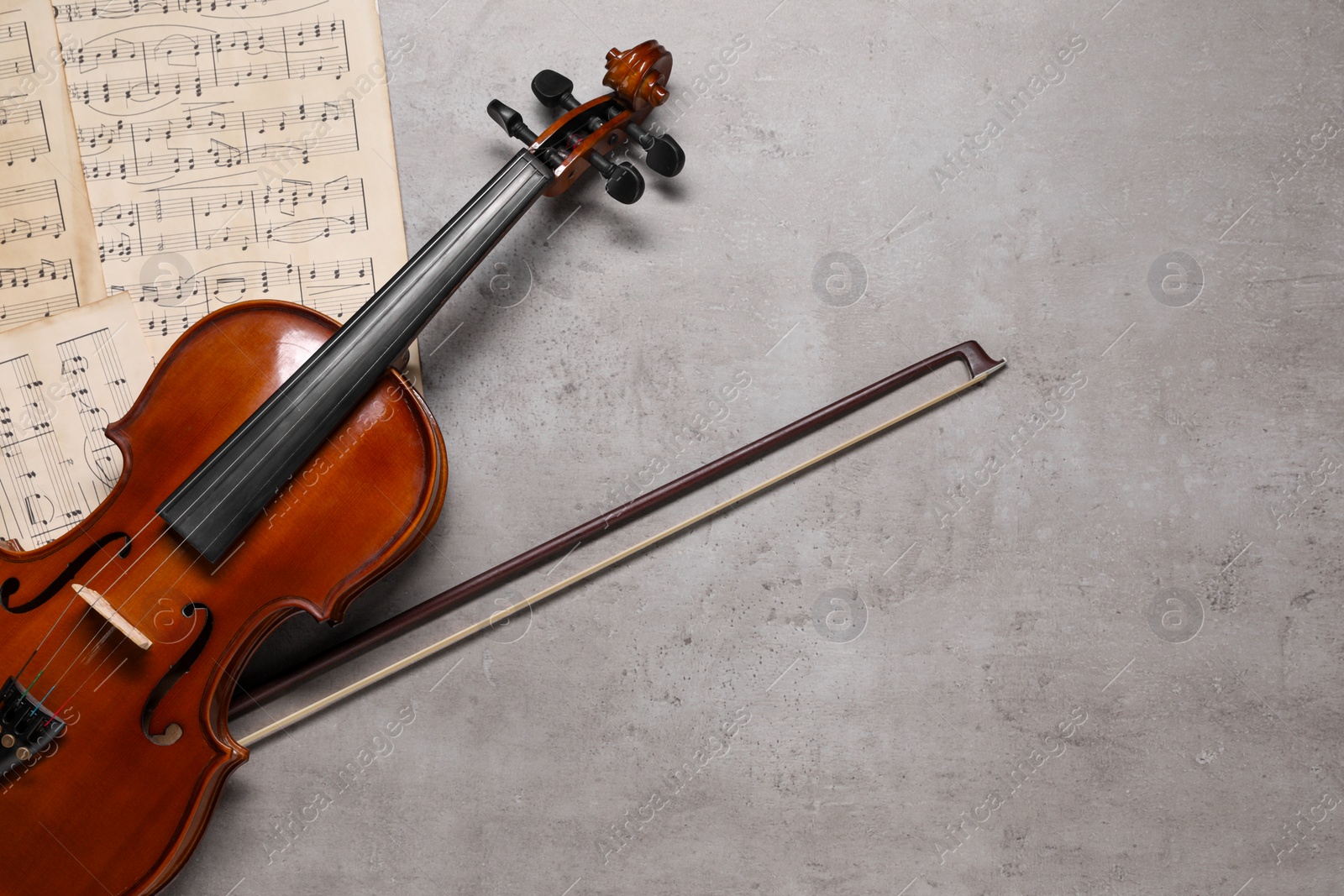 Photo of Violin, bow and music sheets on grey table, top view. Space for text