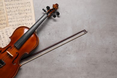 Violin, bow and music sheets on grey table, top view. Space for text