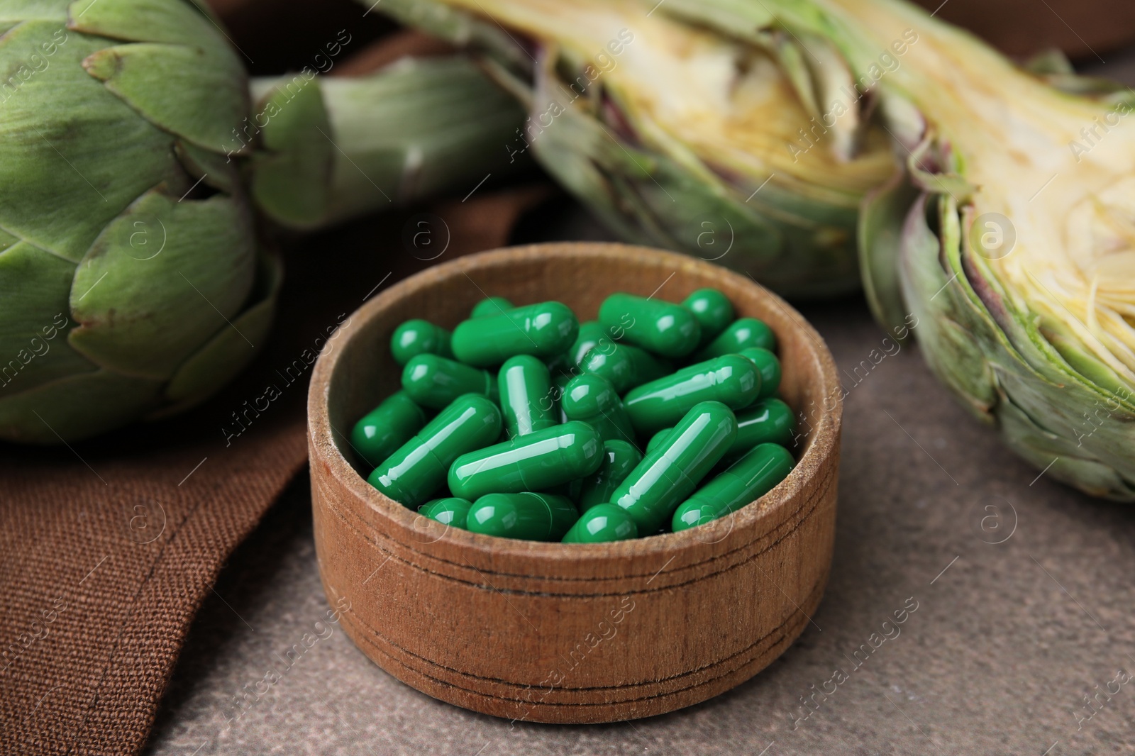 Photo of Bowl with pills and fresh artichokes on brown table, closeup