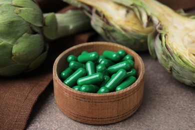 Bowl with pills and fresh artichokes on brown table, closeup