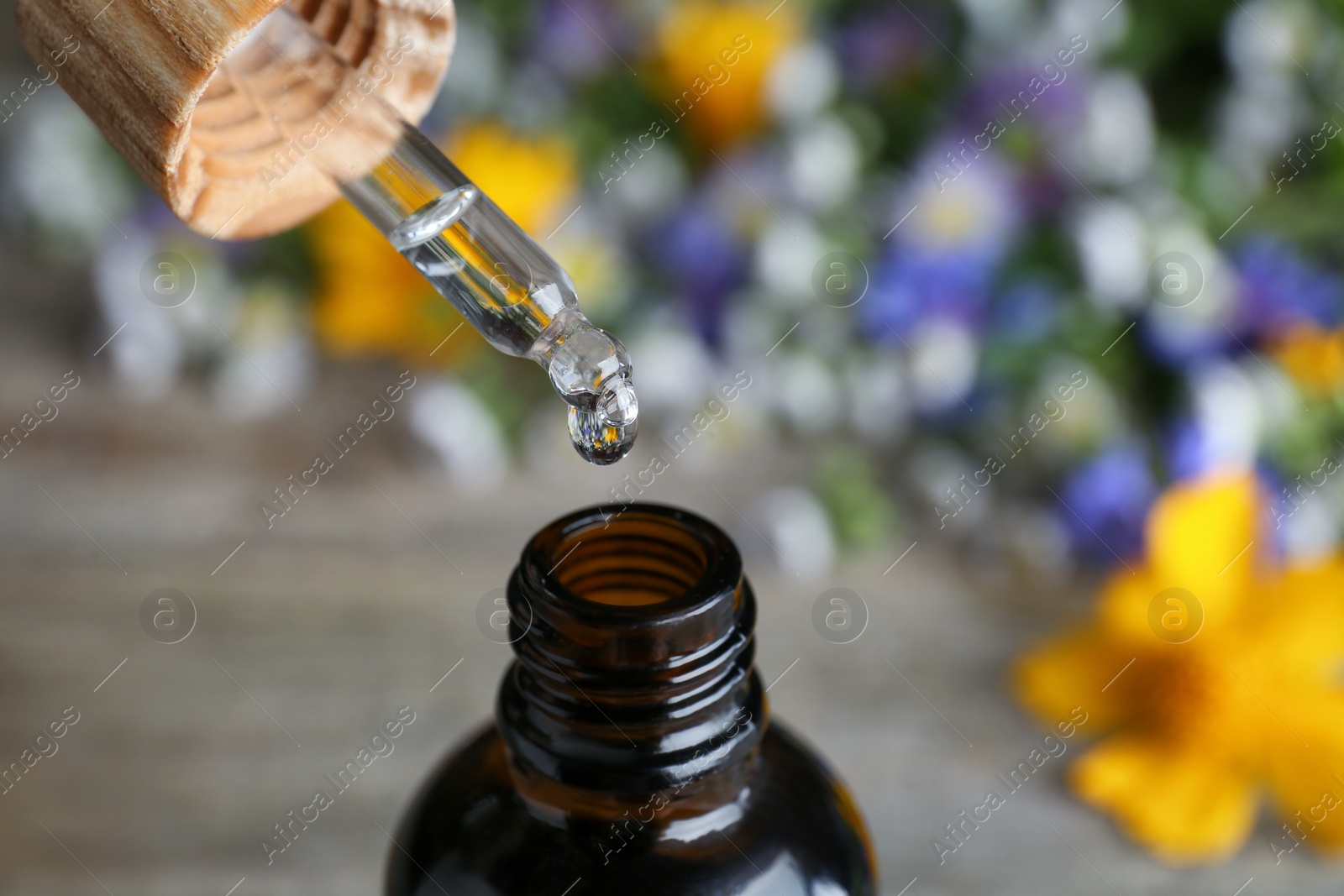 Photo of Dripping essential oil from pipette into bottle on table, closeup