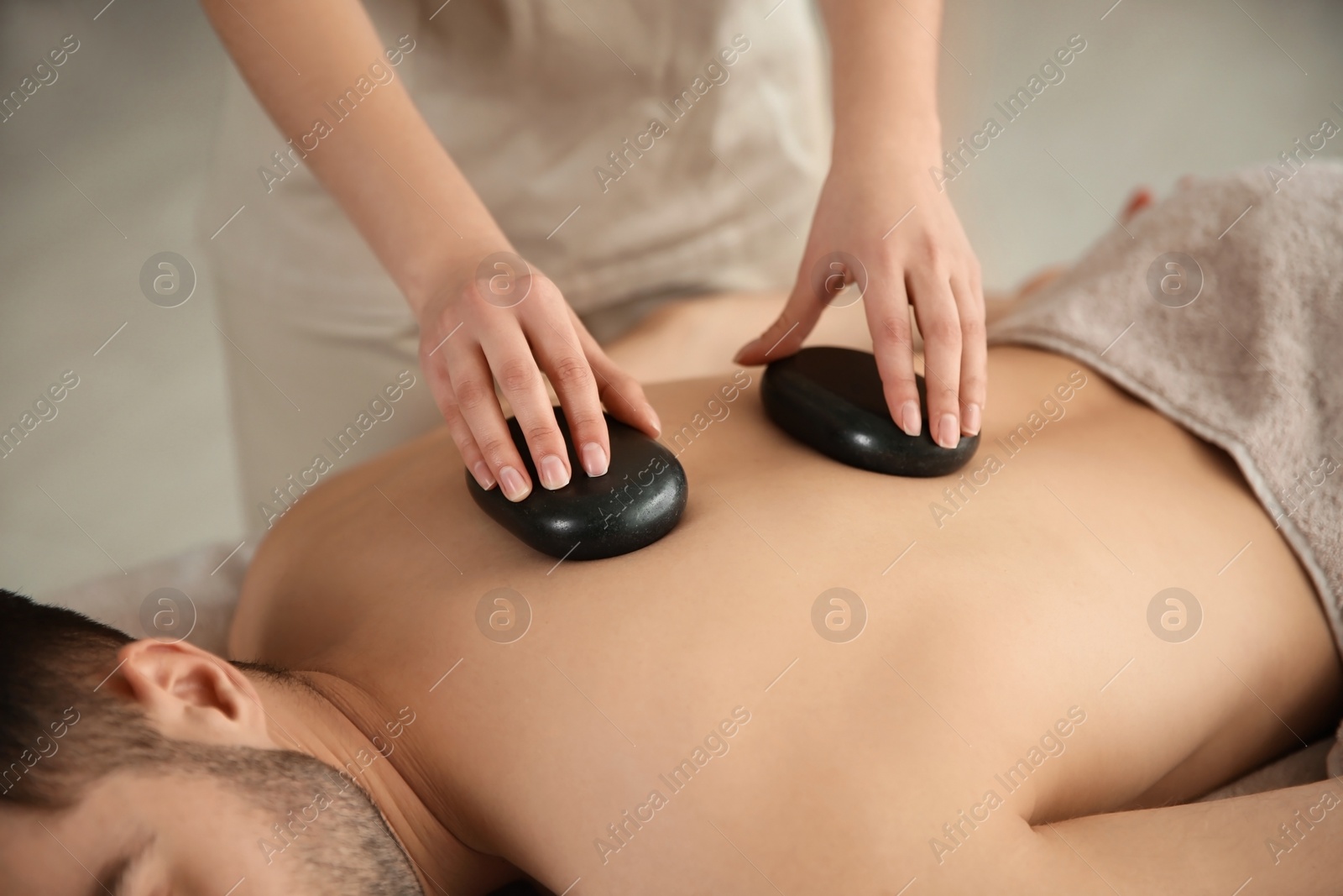 Photo of Man receiving hot stone massage in spa salon, closeup