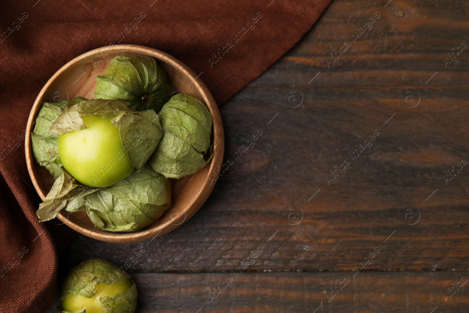 Photo of Fresh green tomatillos with husk in bowl on wooden table, top view. Space for text