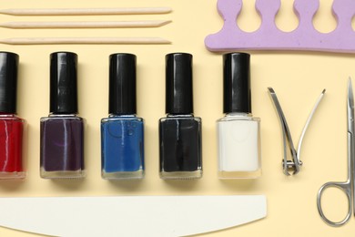 Photo of Nail polishes and set of pedicure tools on beige background, flat lay