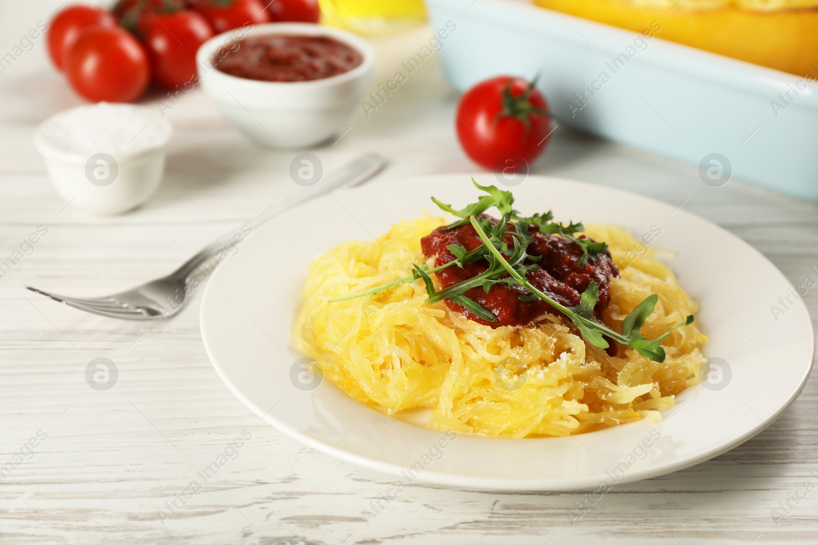 Photo of Tasty spaghetti squash with tomato sauce and arugula served on white wooden table, closeup