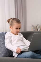 Photo of Little girl using laptop on sofa at home. Internet addiction