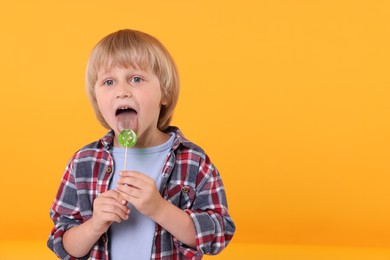Cute little boy licking lollipop on orange background, space for text
