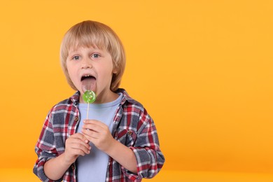 Photo of Cute little boy licking lollipop on orange background, space for text