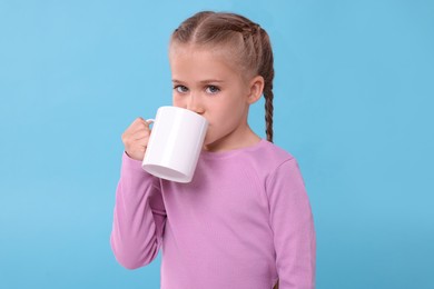 Photo of Cute girl drinking from white ceramic mug on light blue background