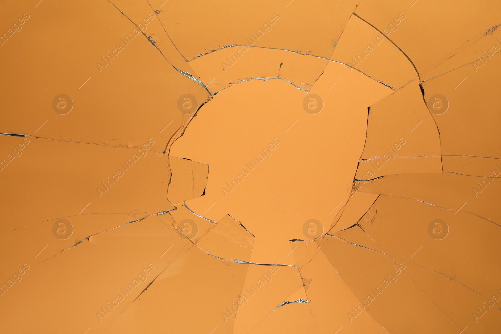 Photo of Closeup view of broken glass with cracks on orange background