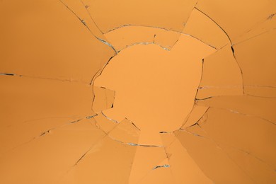Photo of Closeup view of broken glass with cracks on orange background