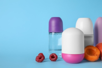 Photo of Different female roll-on deodorants, apricots and raspberries on light blue background. Space for text