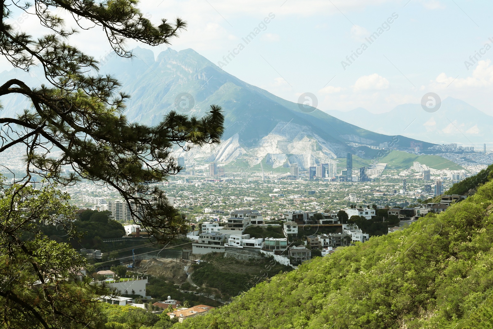 Photo of Picturesque view of trees, buildings and mountains under beautiful sky in city