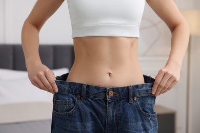 Photo of Slim woman wearing big jeans in room, closeup. Weight loss
