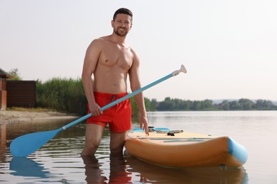 Man with paddle standing near SUP board in water