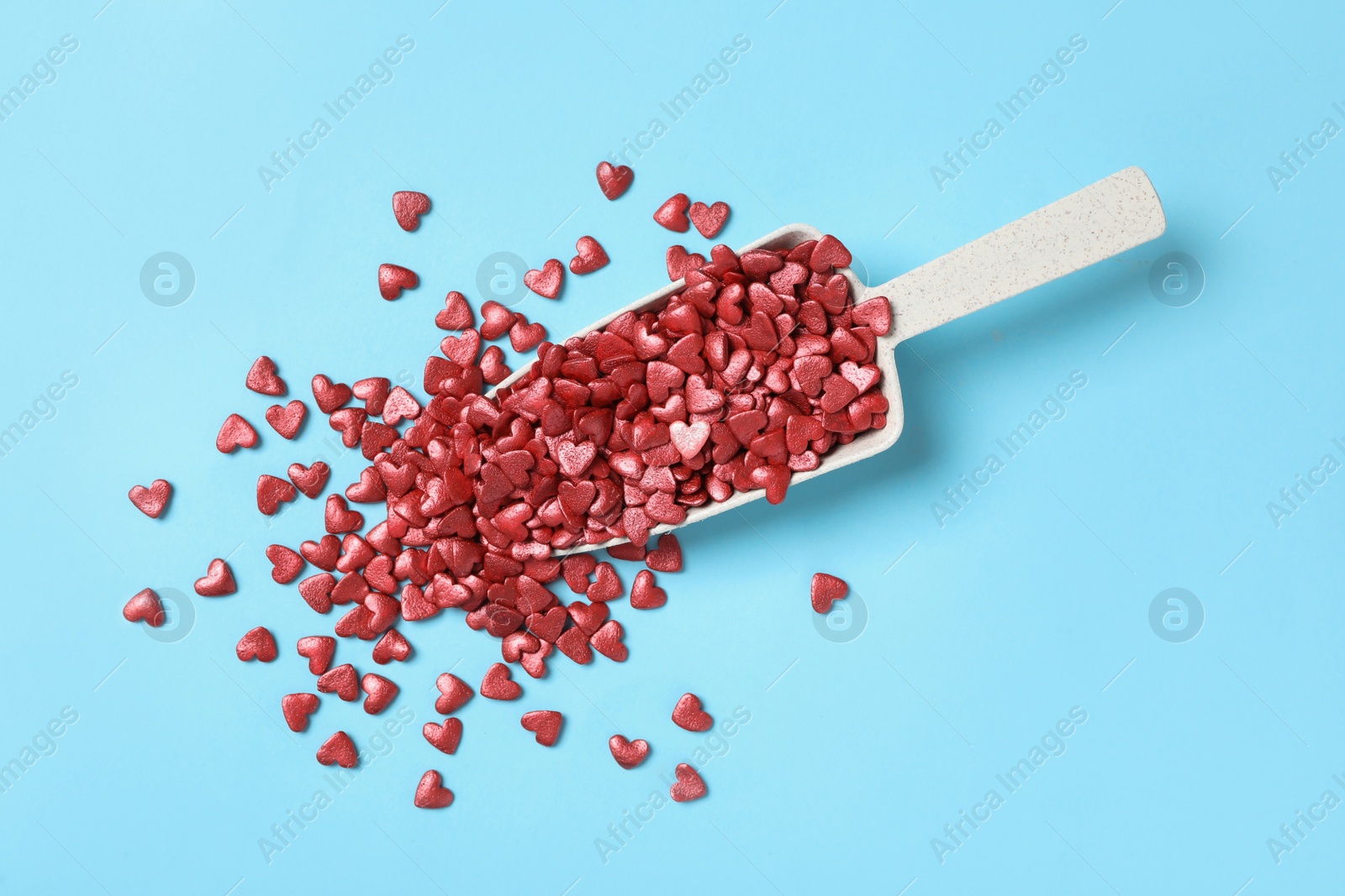 Photo of Bright heart shaped sprinkles and scoop on light blue background, flat lay