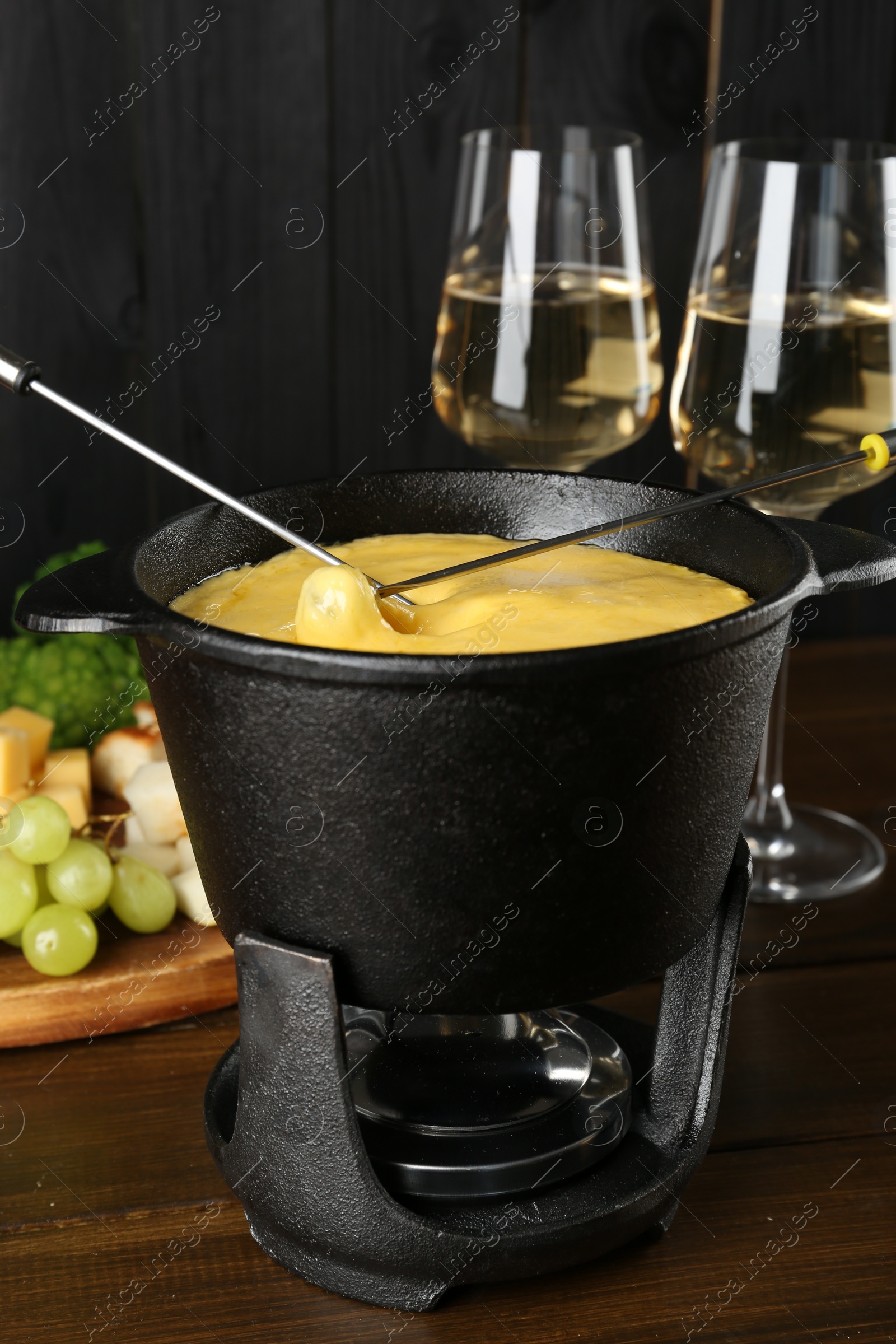Photo of Dipping different products into fondue pot with melted cheese on wooden table
