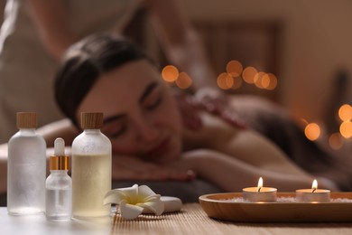 Photo of Spa therapy. Beautiful young woman lying on table during massage in salon, focus on burning candles and cosmetic products