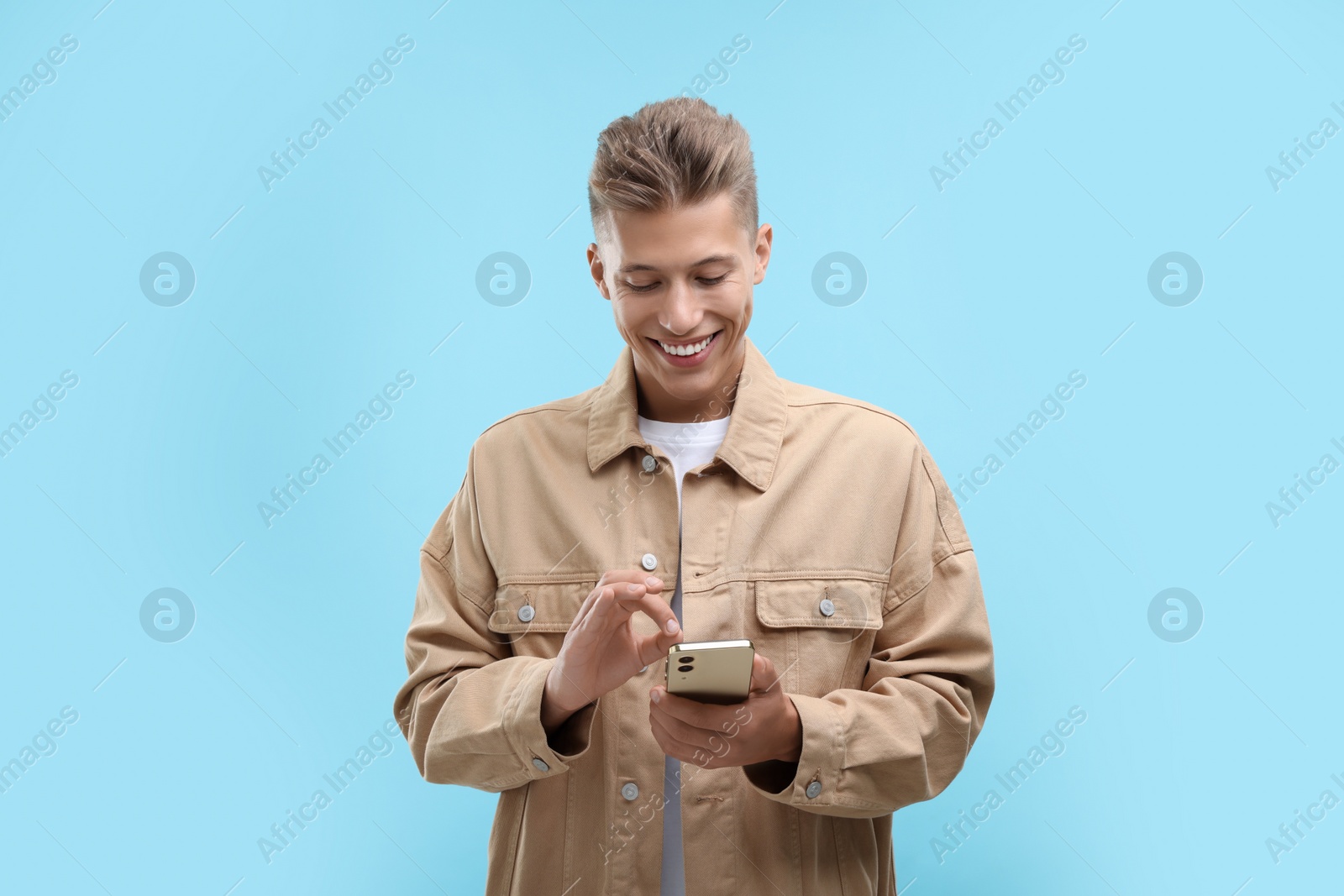 Photo of Happy young man sending message via smartphone on light blue background