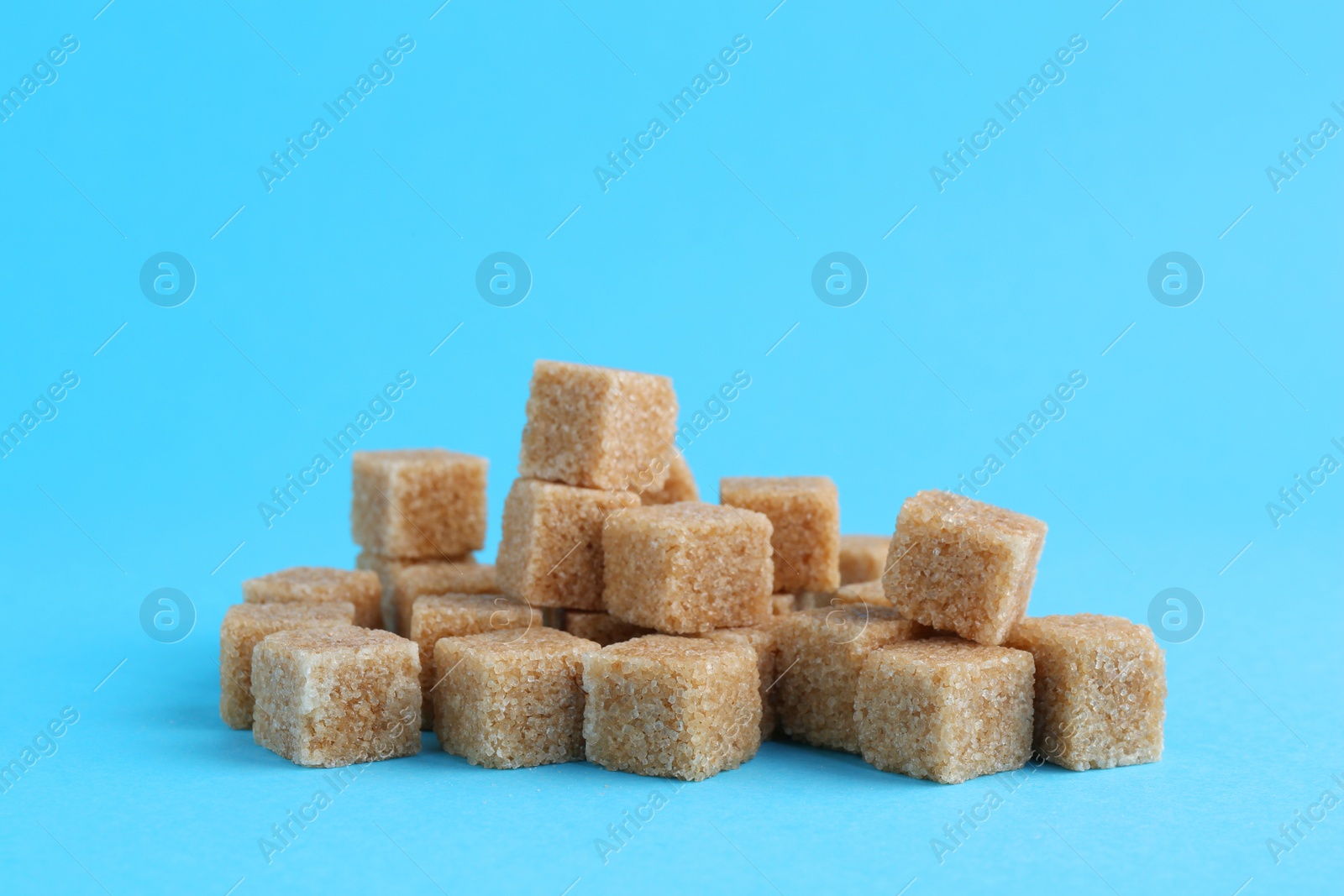 Photo of Pile of brown sugar cubes on light blue background