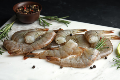 Photo of Fresh raw shrimps with rosemary and pepper on marble board, closeup