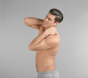 Young man suffering from neck pain on grey background